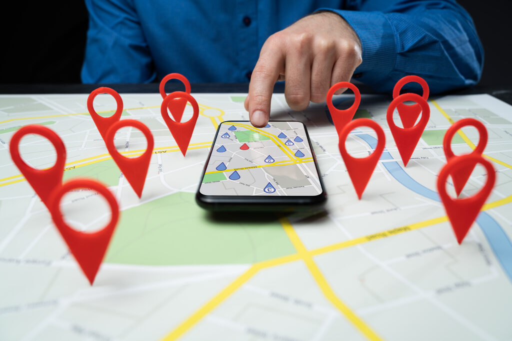 Smartphone mit digitaler Karte und roten Standortmarkierungen auf physischer Straßenkarte