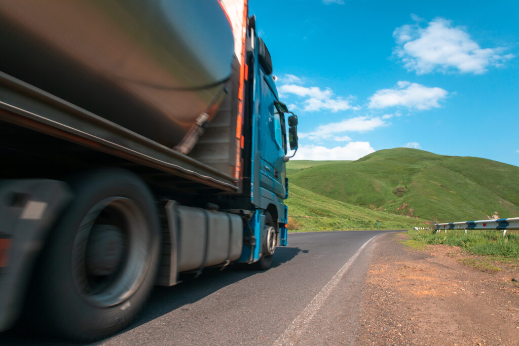 Fahrender LKW auf Landstraße mit grüner Hügellandschaft im Hintergrund