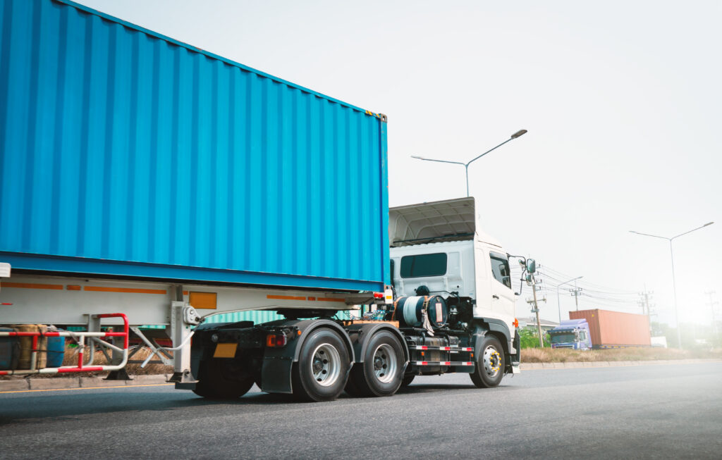 Sattelzug mit blauem Container fährt auf Straße im Logistikbereich bei Tageslicht
