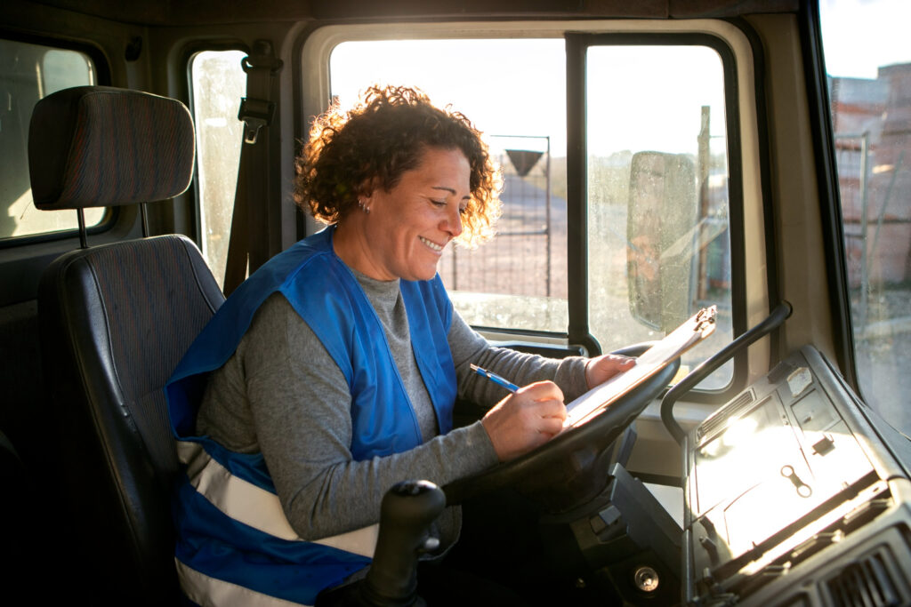 Eine Frau schreibt auf einem Blatt Papier. Sie sitzt in der Kabine ihres LKW